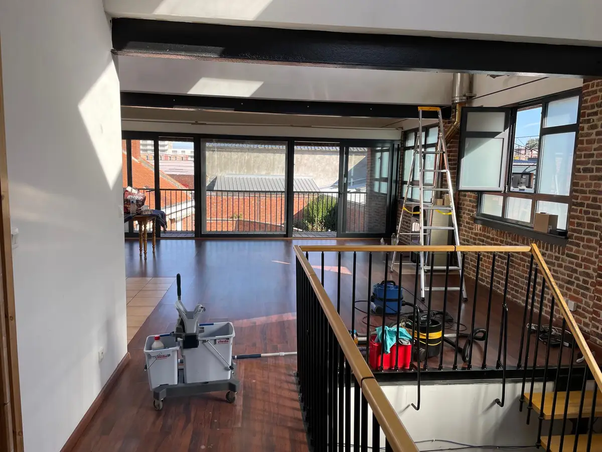 Plateau de bureaux sous charpente, chariot de ménage et aspirateur en cours de passage près de l’escalier
