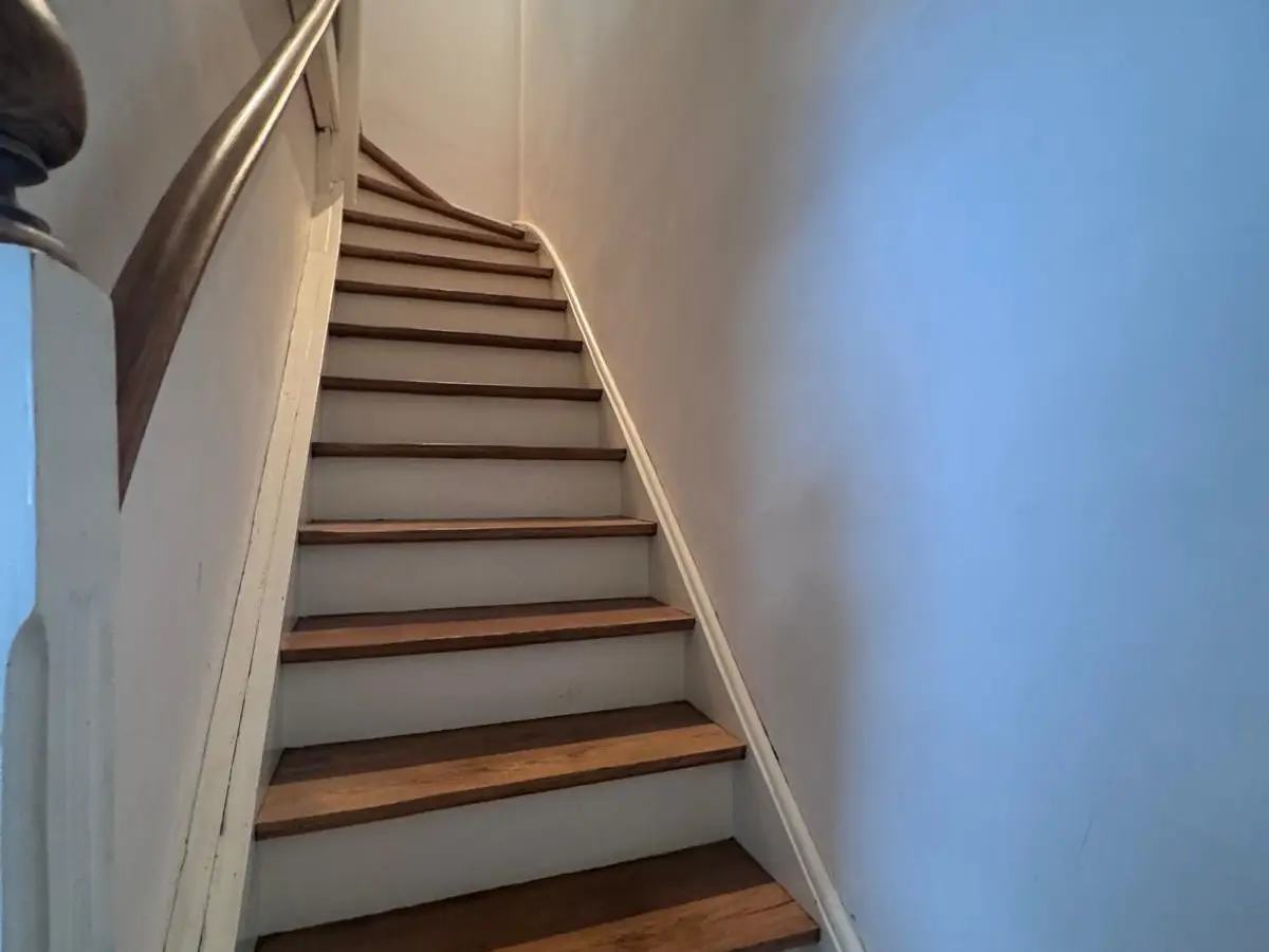 Escalier en bois d’un logement vide, marches brunes, contremarches blanches, rampe et plinthes propres