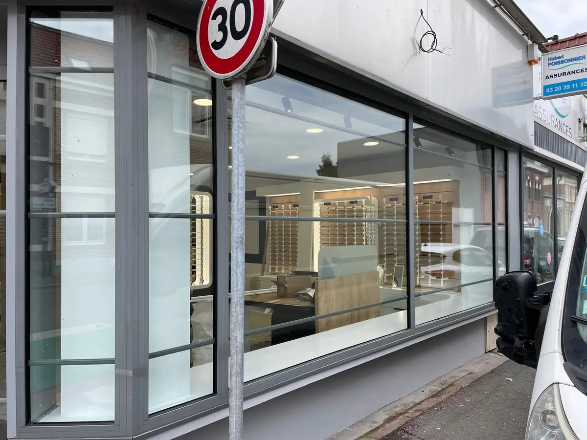 Grande vitrine de magasin aux vitres propres et aux cadres gris, avec des présentoirs visibles à l’intérieur