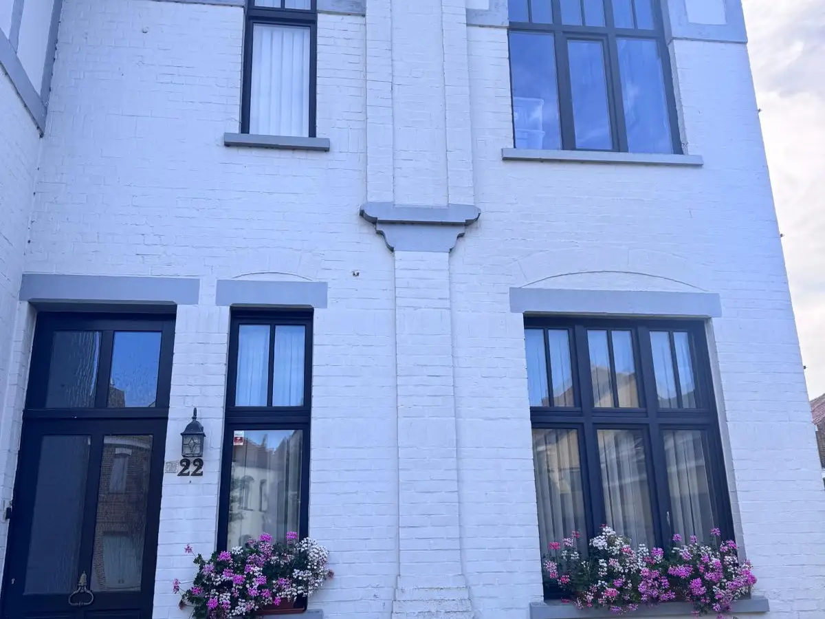 Façade blanche aux fenêtres à petits carreaux et jardinières fleuries