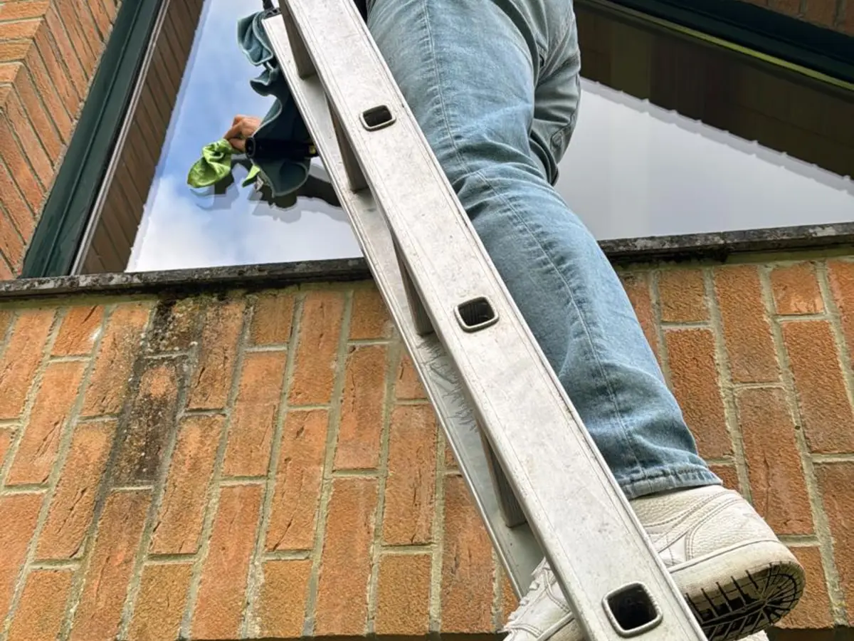 Nettoyage d'une fenêtre de pignon en brique depuis une échelle