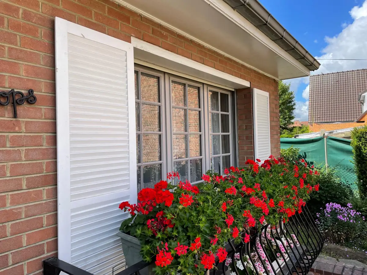 Fenêtre à volets blancs et jardinières fleuries